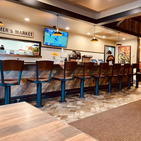 Interior view of Rooster Run Cafe's counter with bar stools, a TV, and a person working.