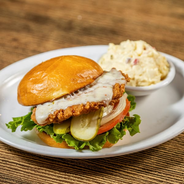 Crispy chicken sandwich with melted cheese, lettuce, tomato, onion, pickles, and a side of potato salad.