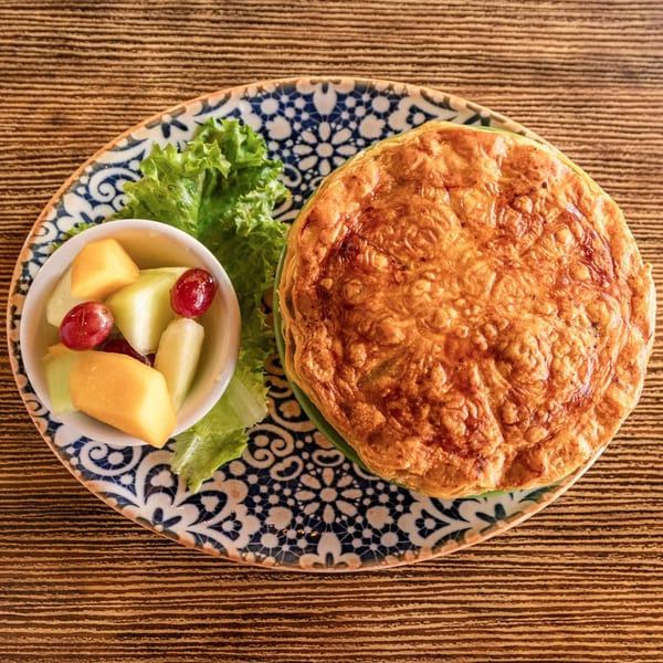 A golden-brown Rooster Run Cafe omelet with a side of fruit and lettuce on a patterned plate.