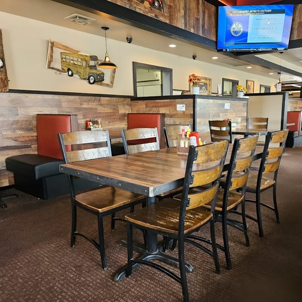Interior of Rooster Run Cafe with wooden tables and chairs, red booths, and a TV screen showing sports.