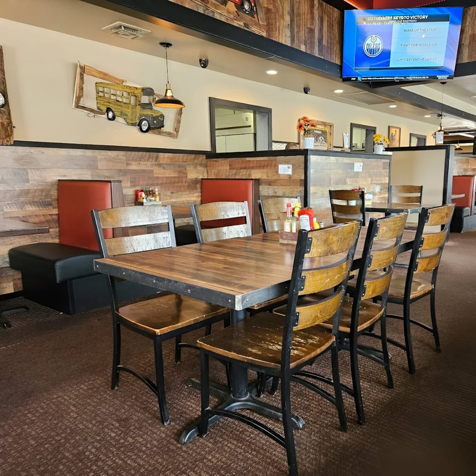 Interior of Rooster Run Cafe with wooden tables and chairs, red booths, and a TV screen showing sports.