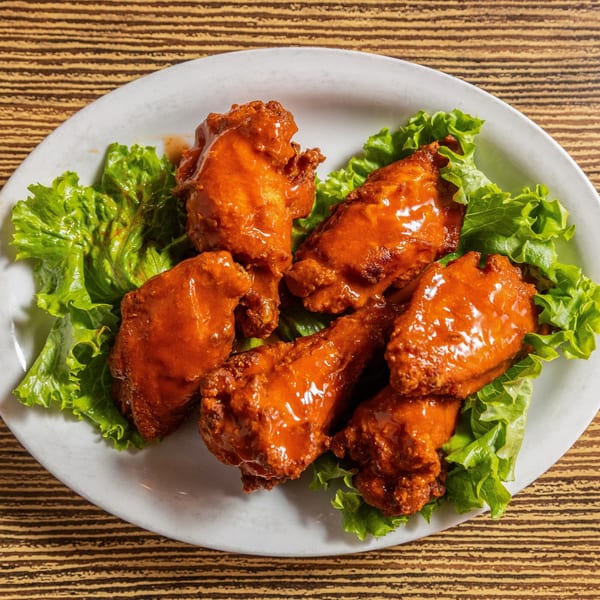 Five Rooster Run Cafe buffalo wings coated in orange sauce, served on a bed of green lettuce.
