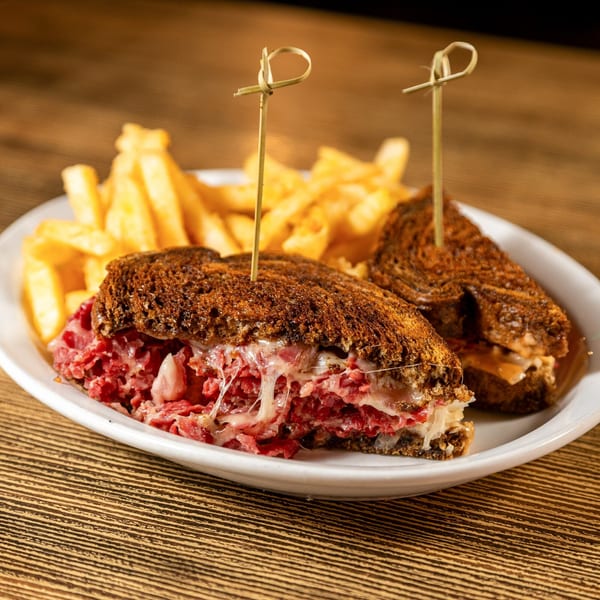 Rooster Run Cafe's Reuben sandwich, cut in half, with melted cheese and fries on a white plate.