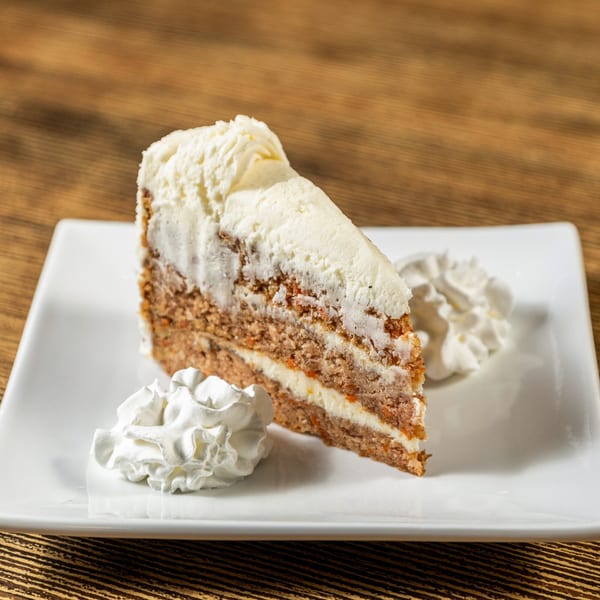 A slice of layered carrot cake with white frosting and whipped cream on a white plate.